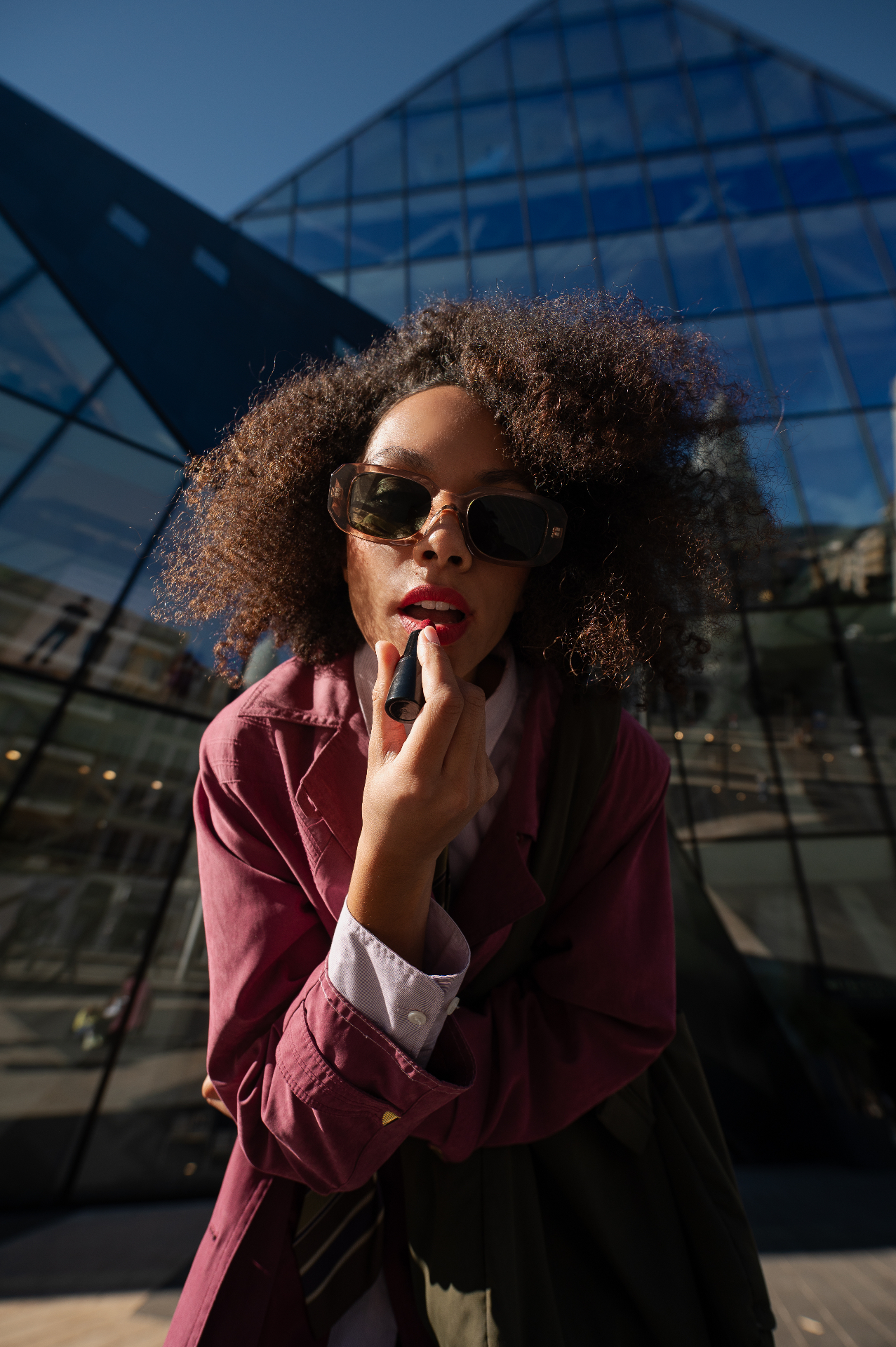 Portrait éditorial d'une femme appliquant un rouge à lèvres devant une architecture de verre